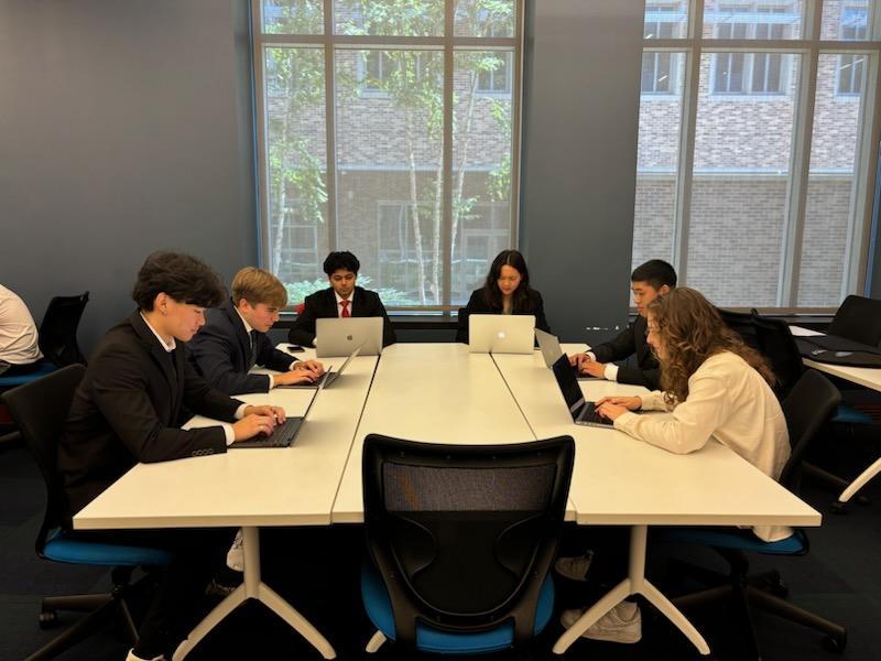 The team of six Code+ students sit around a table, working hard at their computers. From left to right, we have Oliver, Ciaran, Divyansh, Kayla, Andrew, and Phoebe.